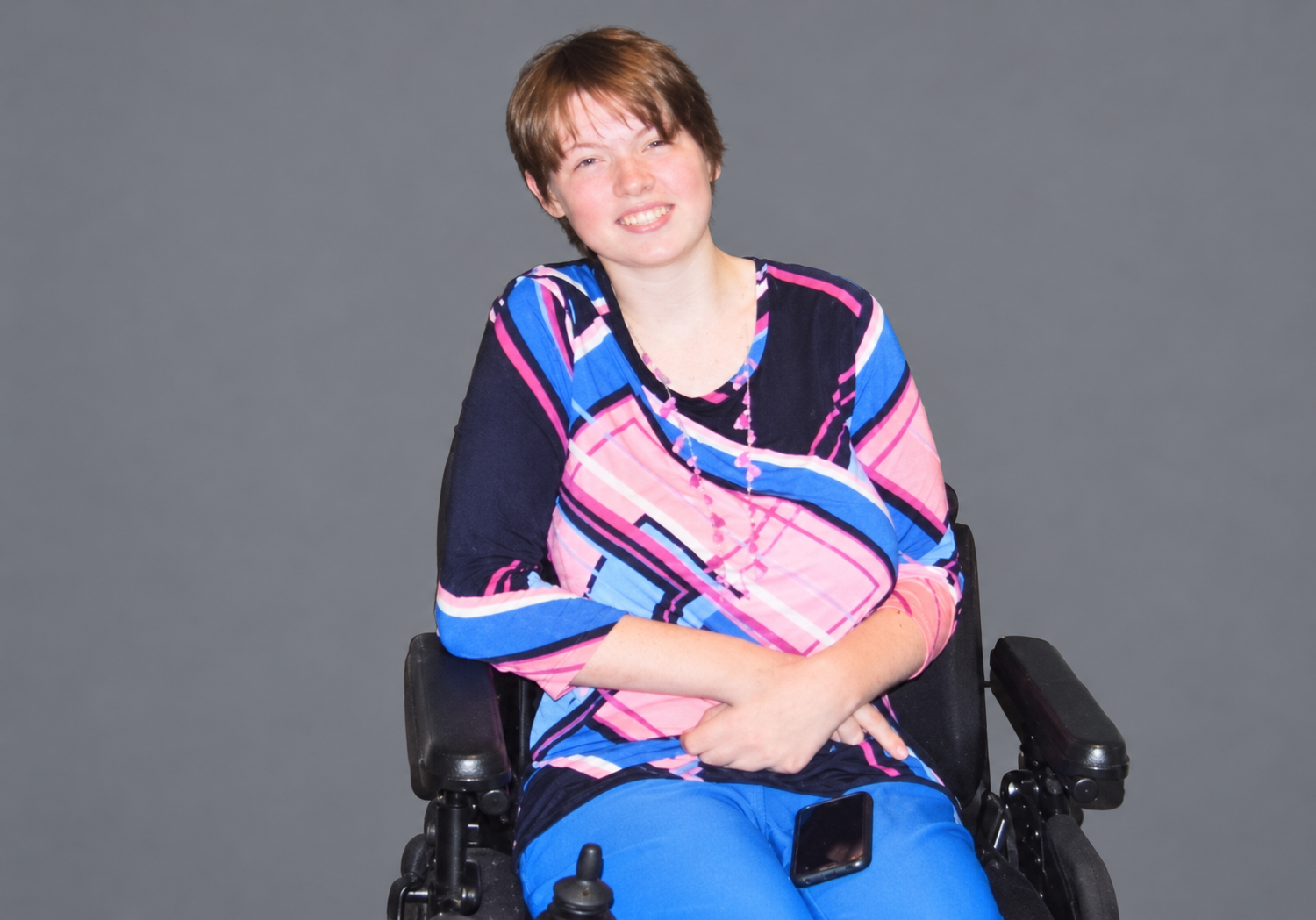 Abbey Davis seated in her power wheelchair against a plain gray background